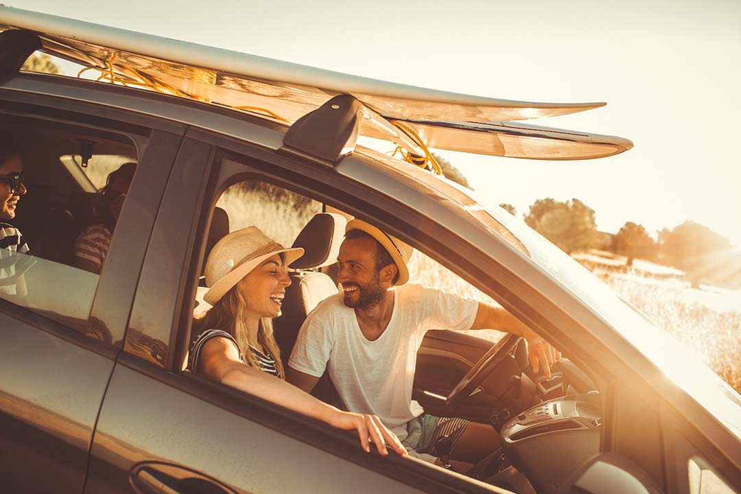 a couple inside of a car with a surfboard on the rack